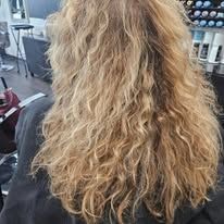 A woman with long blonde curly hair is sitting in a chair in a salon.