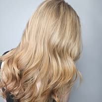 A woman with long blonde hair is standing in front of a white wall.