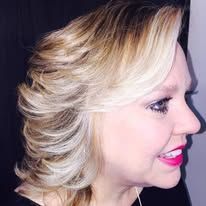 A woman with blonde hair and red lipstick is smiling.