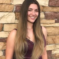 A woman with long hair is smiling in front of a brick wall.