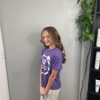 A young girl in a purple shirt is standing in a room.