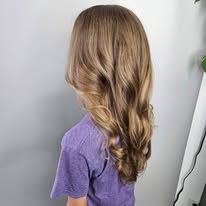 A little girl with long brown hair is wearing a purple shirt.