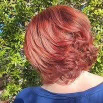 A woman with red hair is wearing a blue shirt and standing in front of a bush.