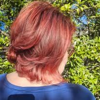 A woman with red hair is wearing a blue shirt and has her hair in a bun.