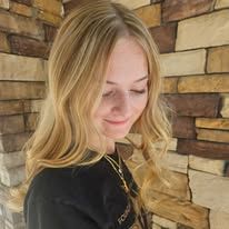 A woman with blonde hair is standing in front of a brick wall.