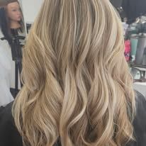 A woman with long blonde hair is sitting in a chair in front of a mannequin head.