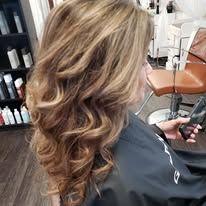 A woman is getting her hair done in a salon while holding a cell phone.