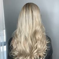 A woman with long blonde hair is standing in front of a window.