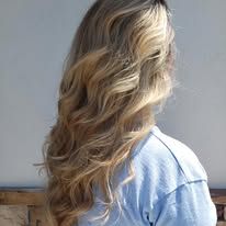 A woman with long blonde wavy hair is wearing a blue shirt.