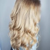 A woman with long blonde hair is standing in front of a wall.