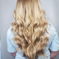 A woman with long blonde wavy hair is wearing a light blue shirt.
