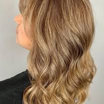 A woman with long wavy blonde hair is wearing a black shirt.