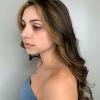 A woman with long brown hair and blonde highlights is wearing a blue top.