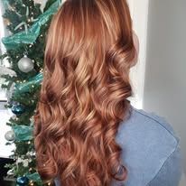 A woman with long red hair is standing in front of a christmas tree.