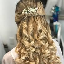 A woman with long blonde hair is wearing a half up half down hairstyle with flowers in her hair.