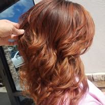 A woman with long red hair is getting her hair done by a hairdresser.