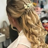 A woman with long blonde hair is wearing a half up half down hairstyle with flowers in her hair.