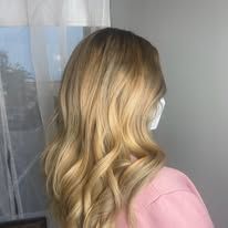 A woman with blonde hair and a pink shirt is standing in front of a window.