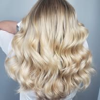 A woman with long blonde wavy hair is wearing a white shirt.