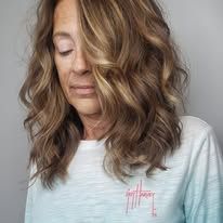 A woman with long wavy brown hair is wearing a white shirt.