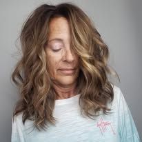 A woman with long brown hair is wearing a white shirt and covering her face with her hair.
