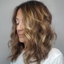 A woman with long wavy brown hair is wearing a white shirt.