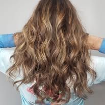 A woman with long wavy hair is standing with her arms outstretched.