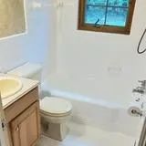 Bathroom with toilet, sink, bathtub, and small window. White walls and light wood trim.