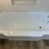 White rectangular bathtub in a bathroom with a tiled wall.
