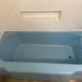 A light blue bathtub, with a drain, is mounted on a white tiled wall.