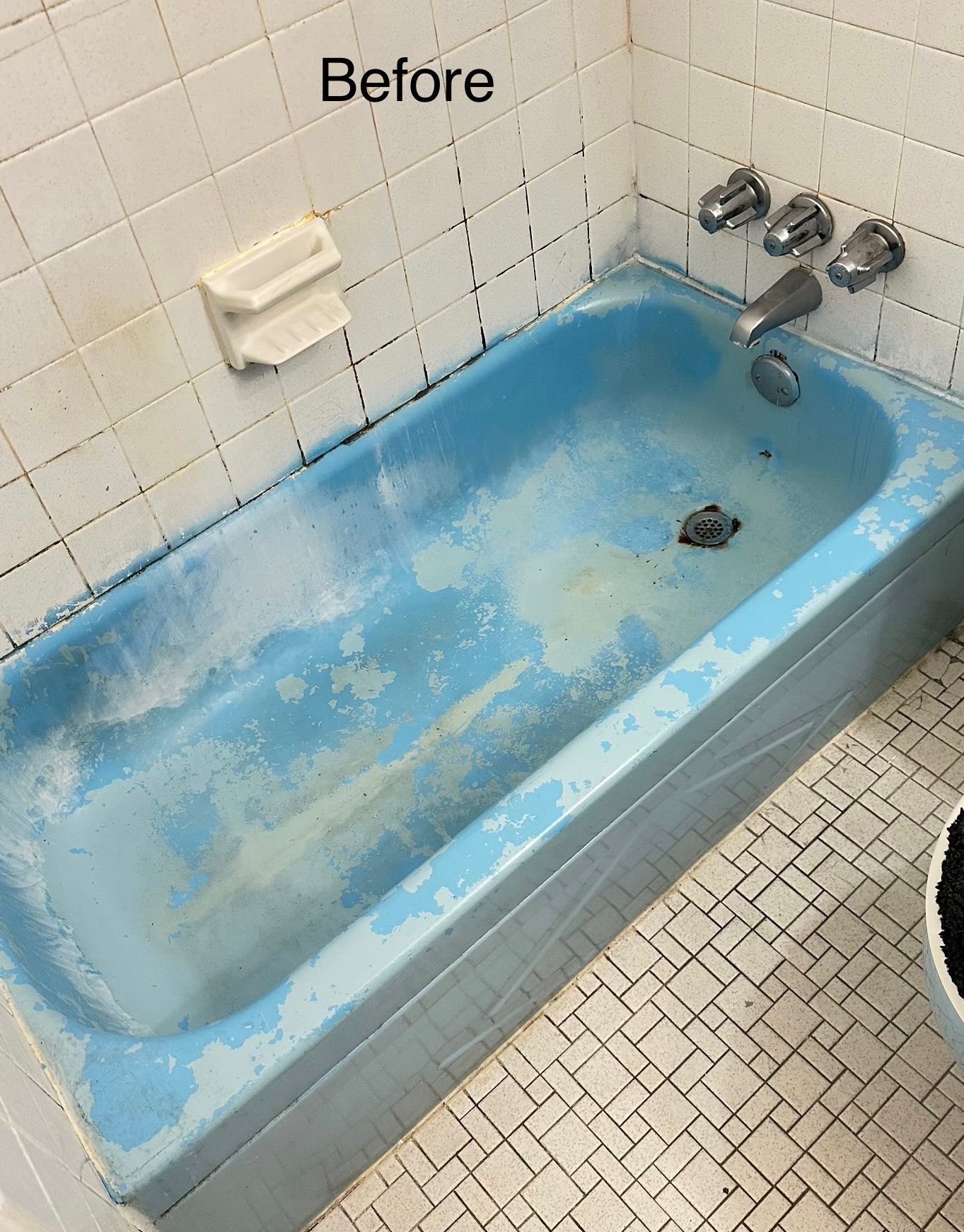 A worn, blue bathtub with peeling paint surrounded by white and gray tiles in a bathroom.