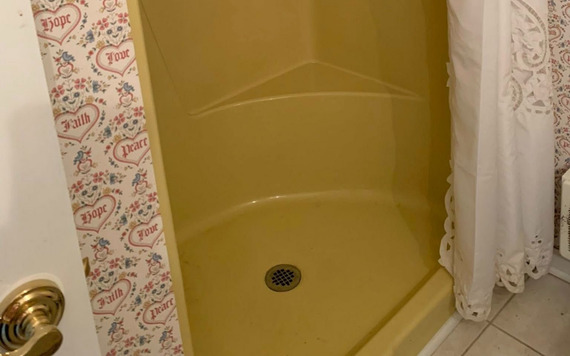 Yellow shower stall with white curtain, in bathroom with patterned wallpaper.