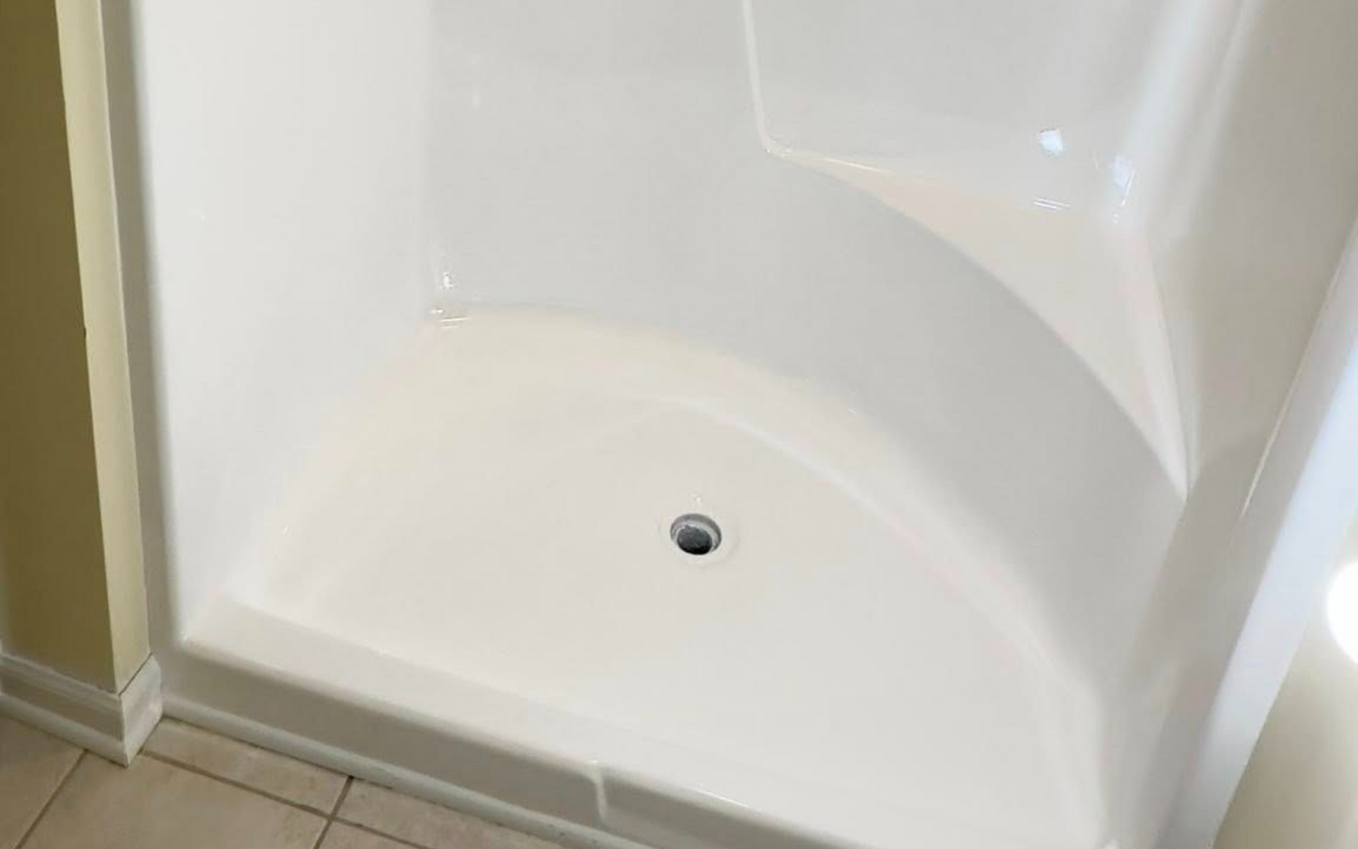 White corner shower stall with built-in seat, shower head, and tile floor.