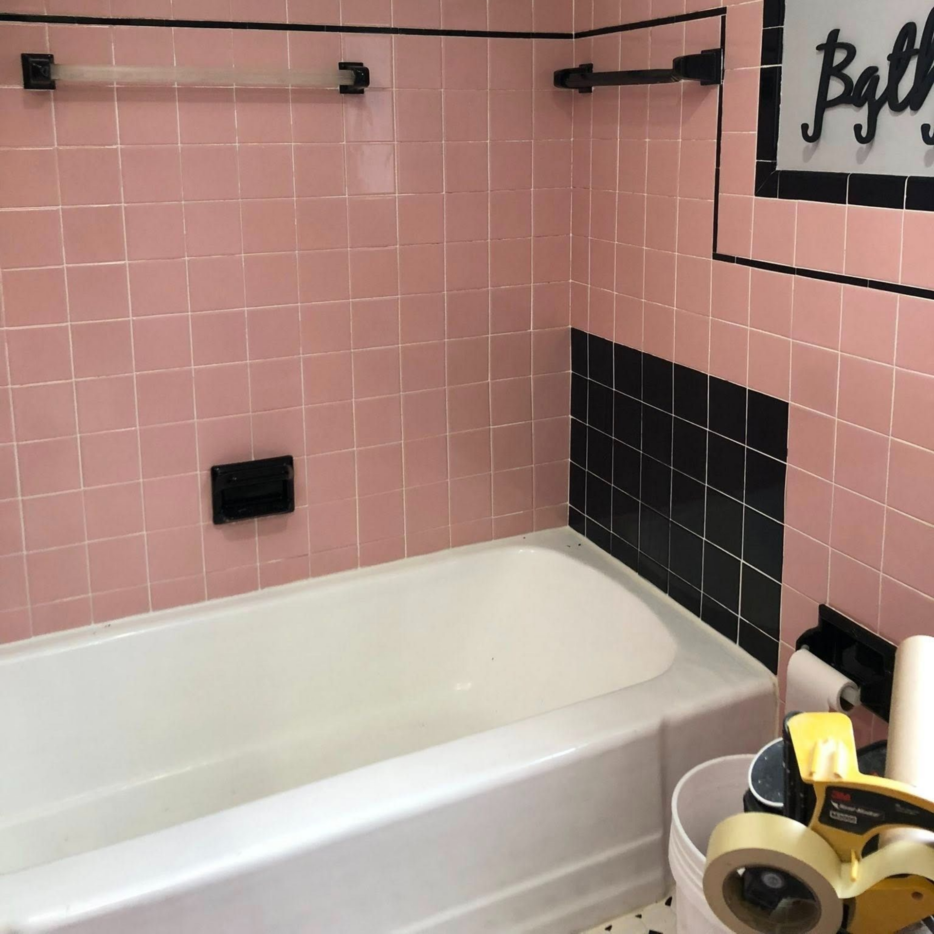 Pink tiled bathroom with black accents and a white tub.