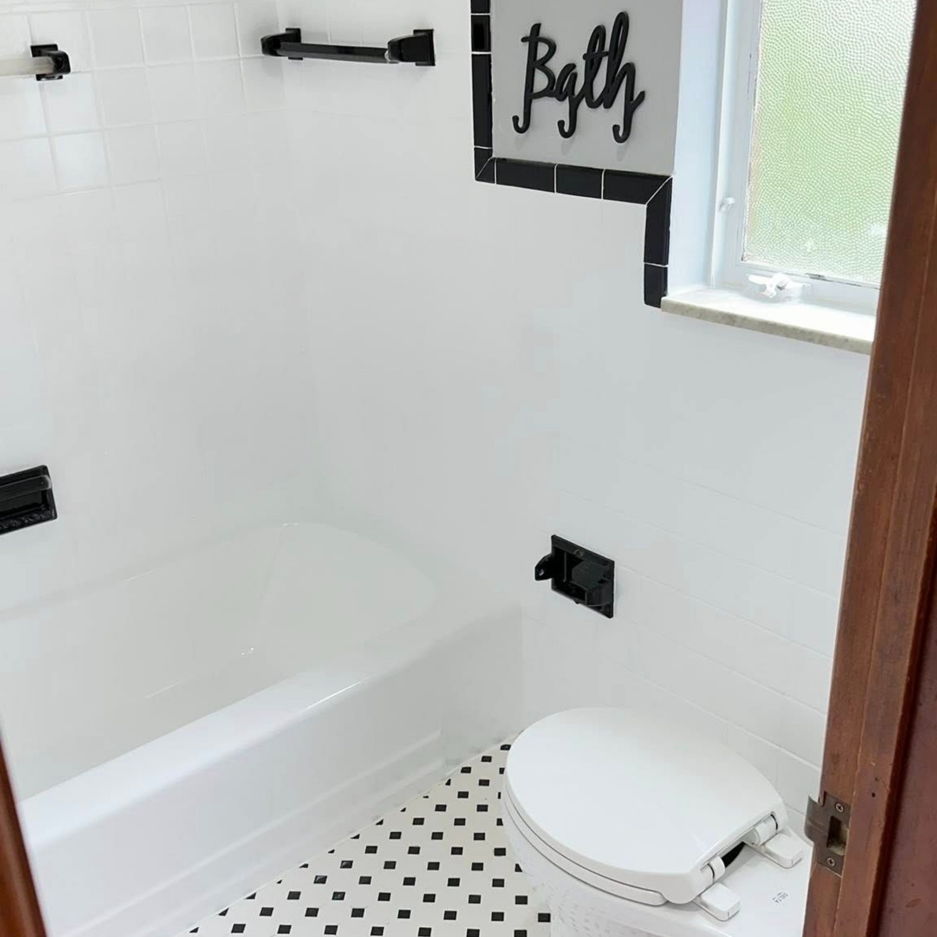 White and black tiled bathroom with a bathtub and toilet; gray walls, black accents.