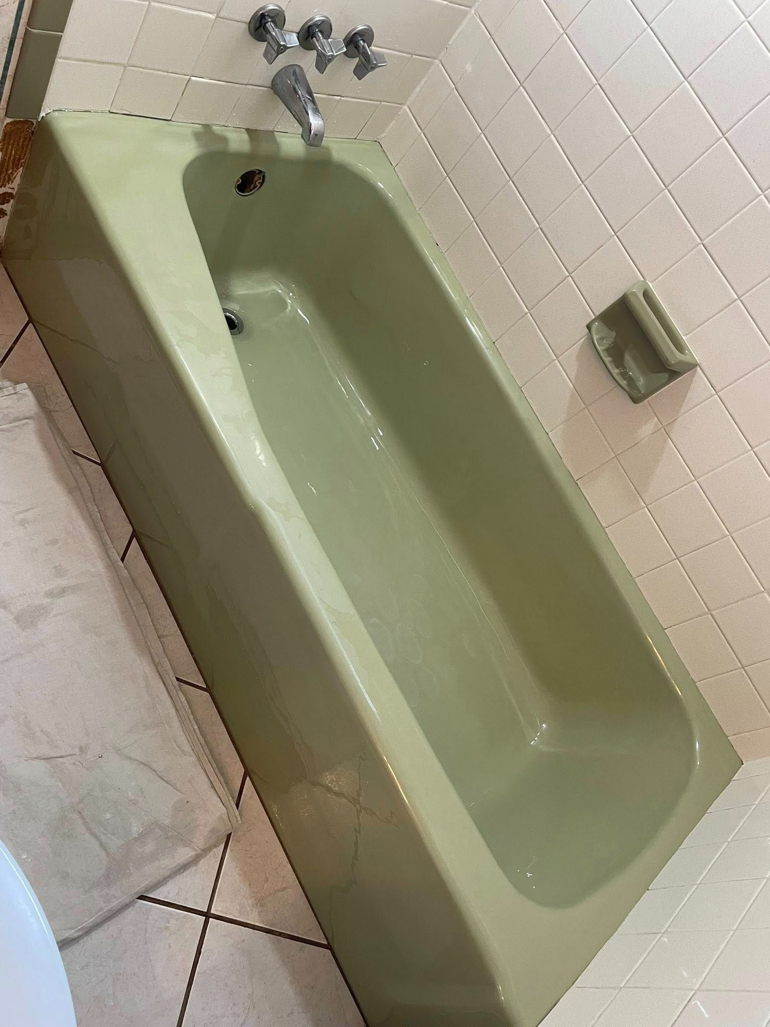 Green bathtub in a tiled bathroom. Soap holder on the wall.
