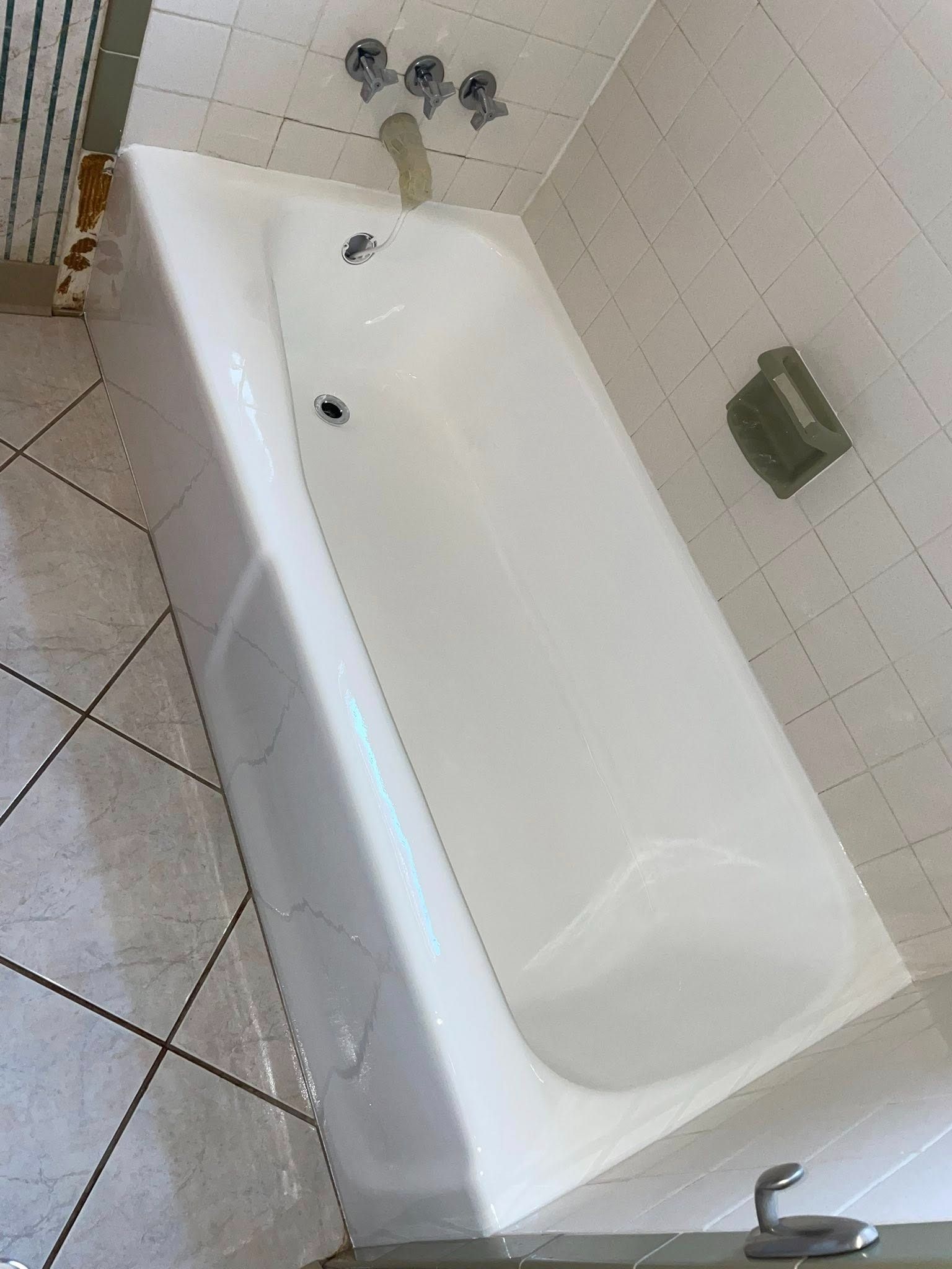 White bathtub in a tiled bathroom with faucet and showerhead. Soap dish on the wall.