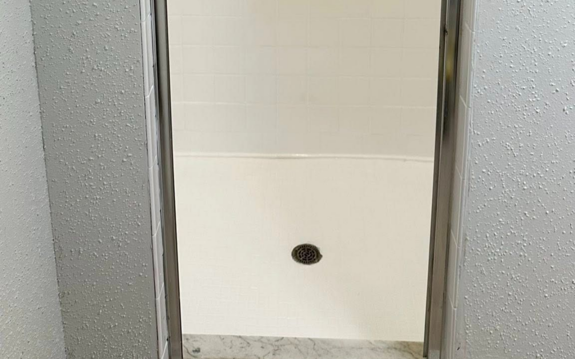 Narrow white-tiled shower with metal ladder on either side, likely under renovation.