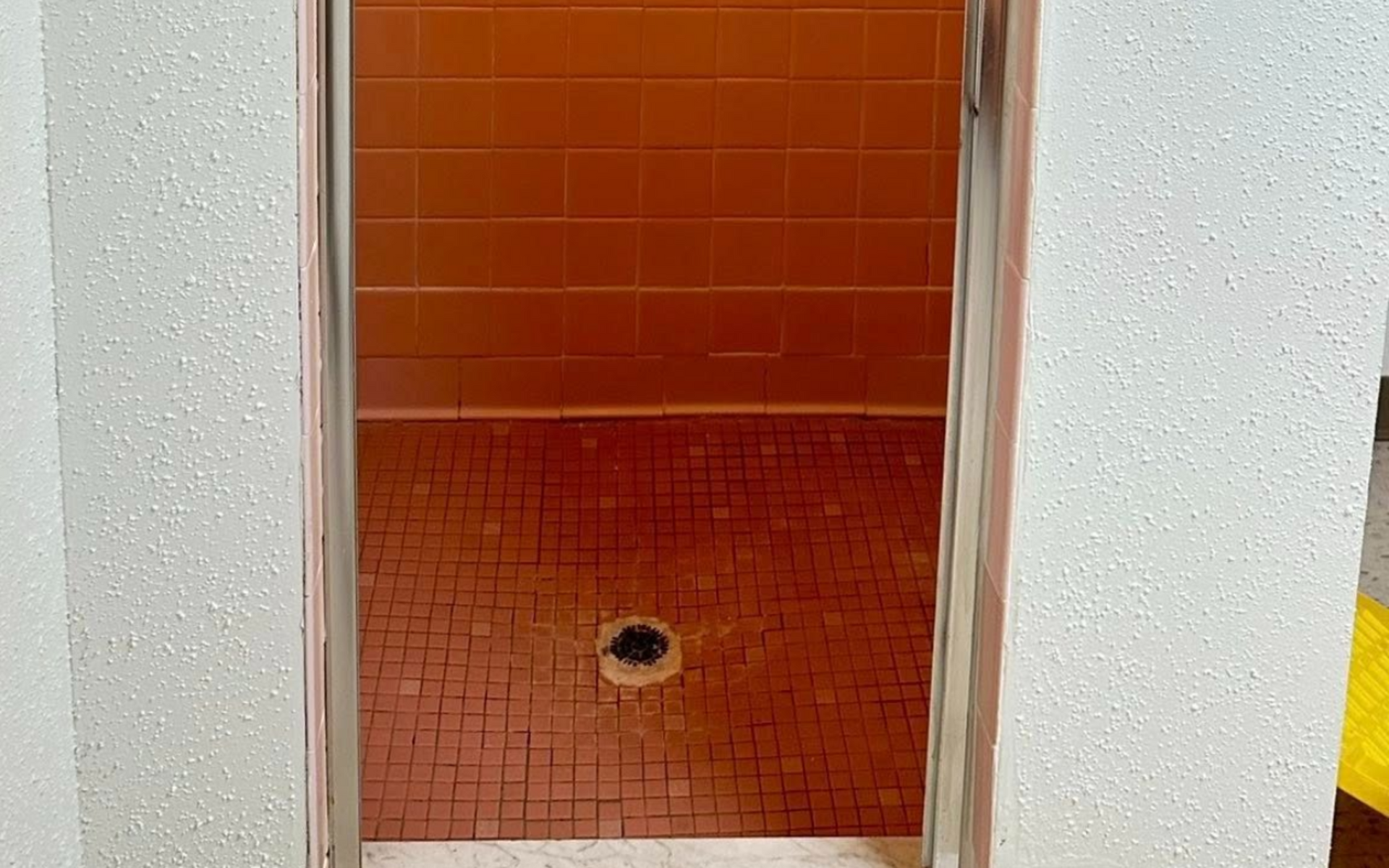 Orange tiled shower stall with a low hanging light.
