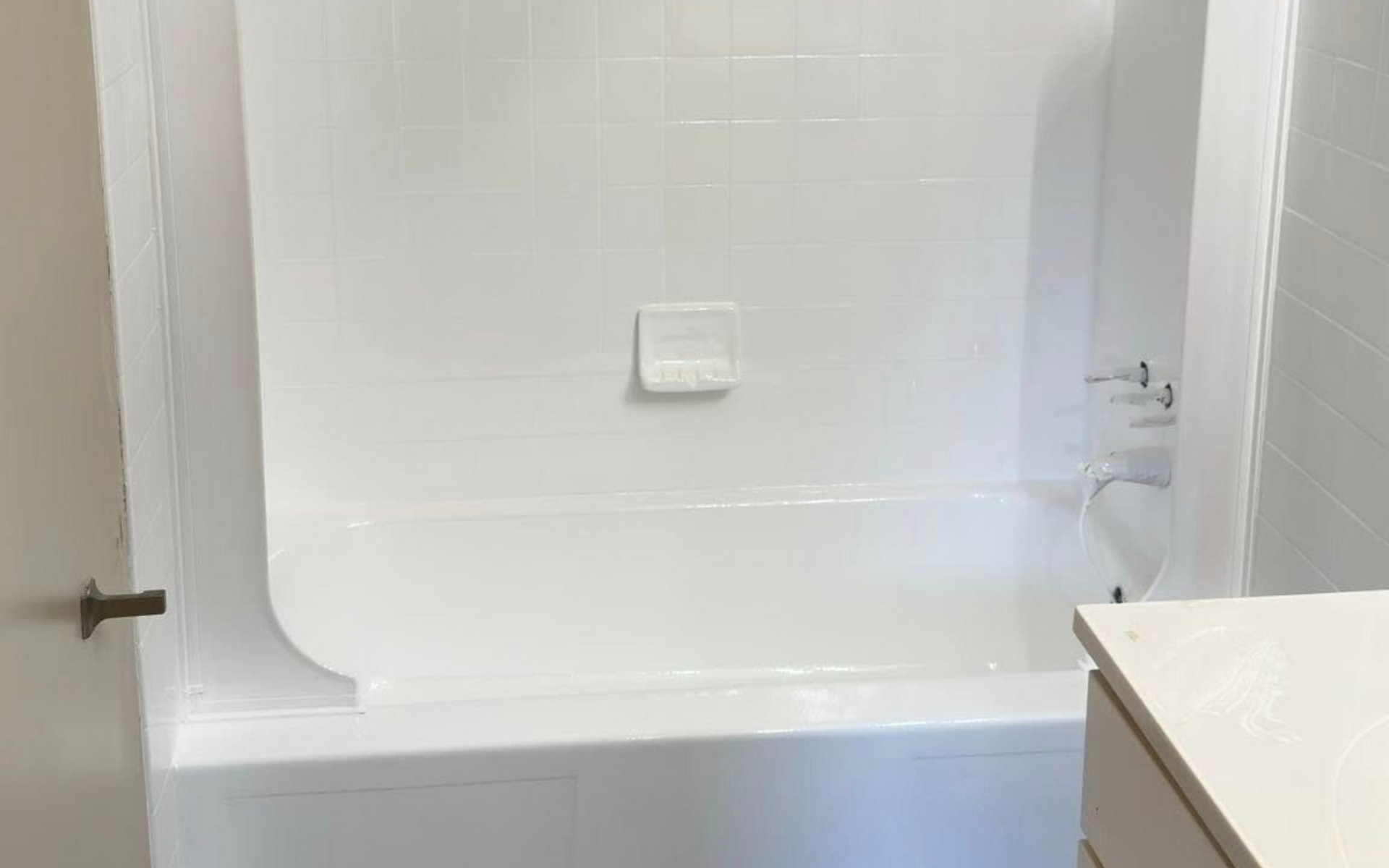 White tiled bathtub and shower with a white vanity to the right. Gray floor.