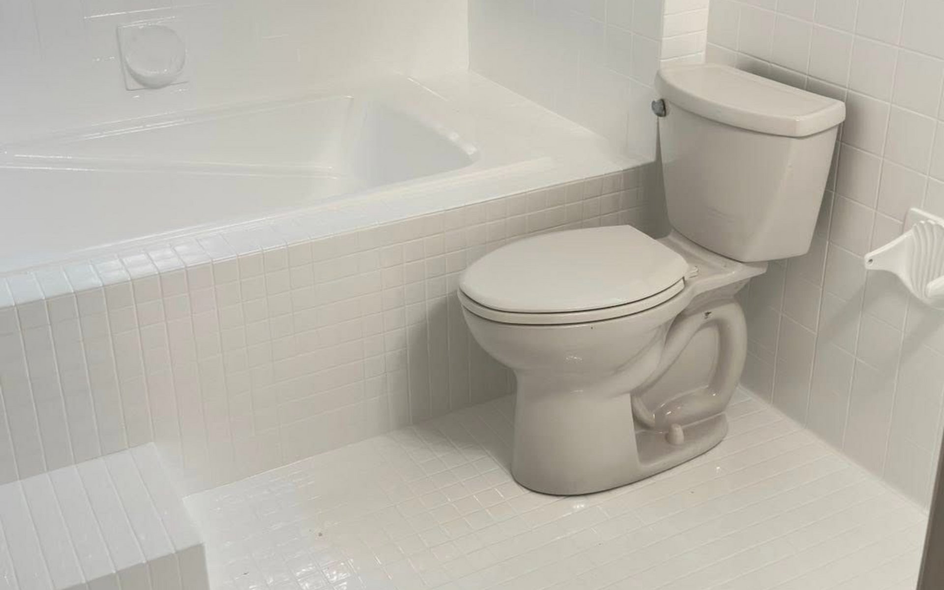 White bathroom with a toilet, bathtub, and tiled walls.