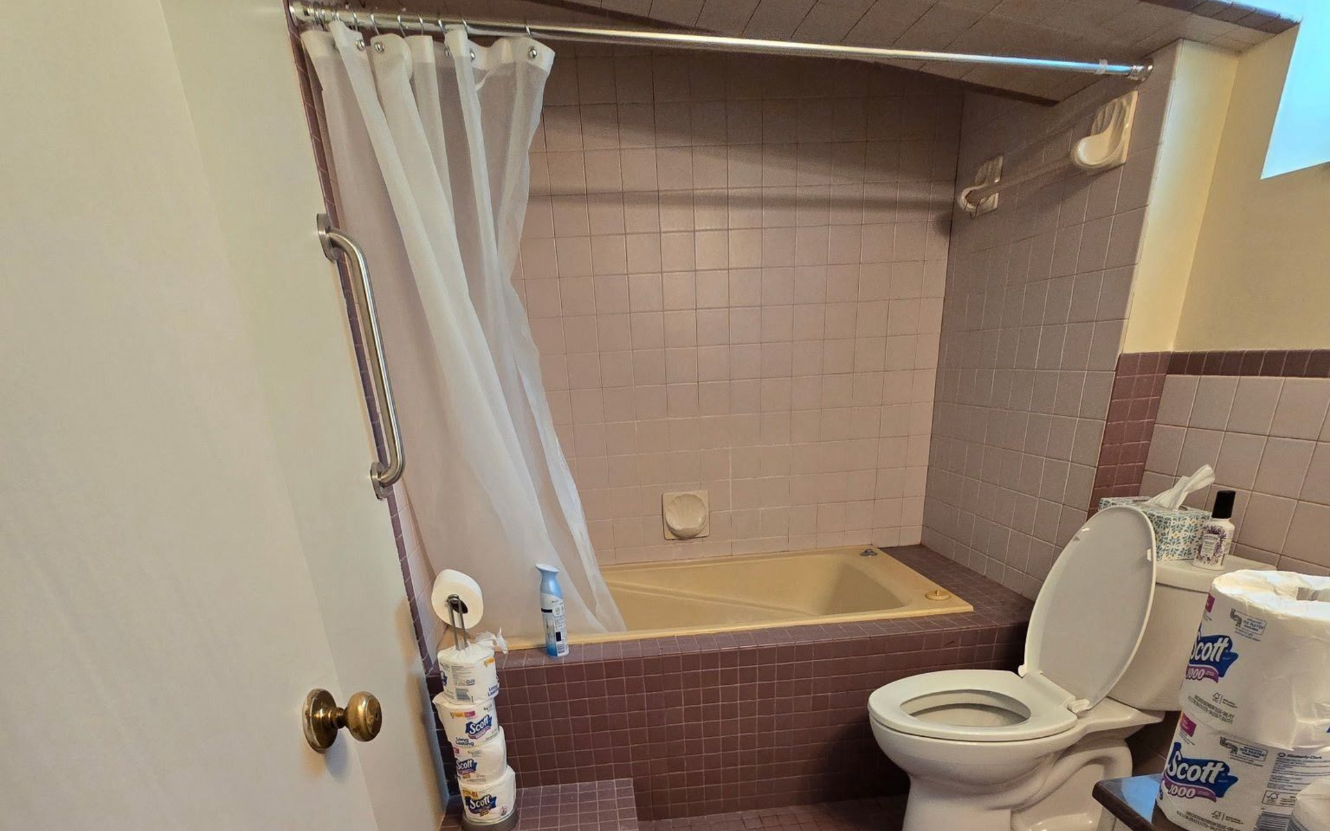 Bathroom with pink tiles, tub, toilet, and a partially open door.