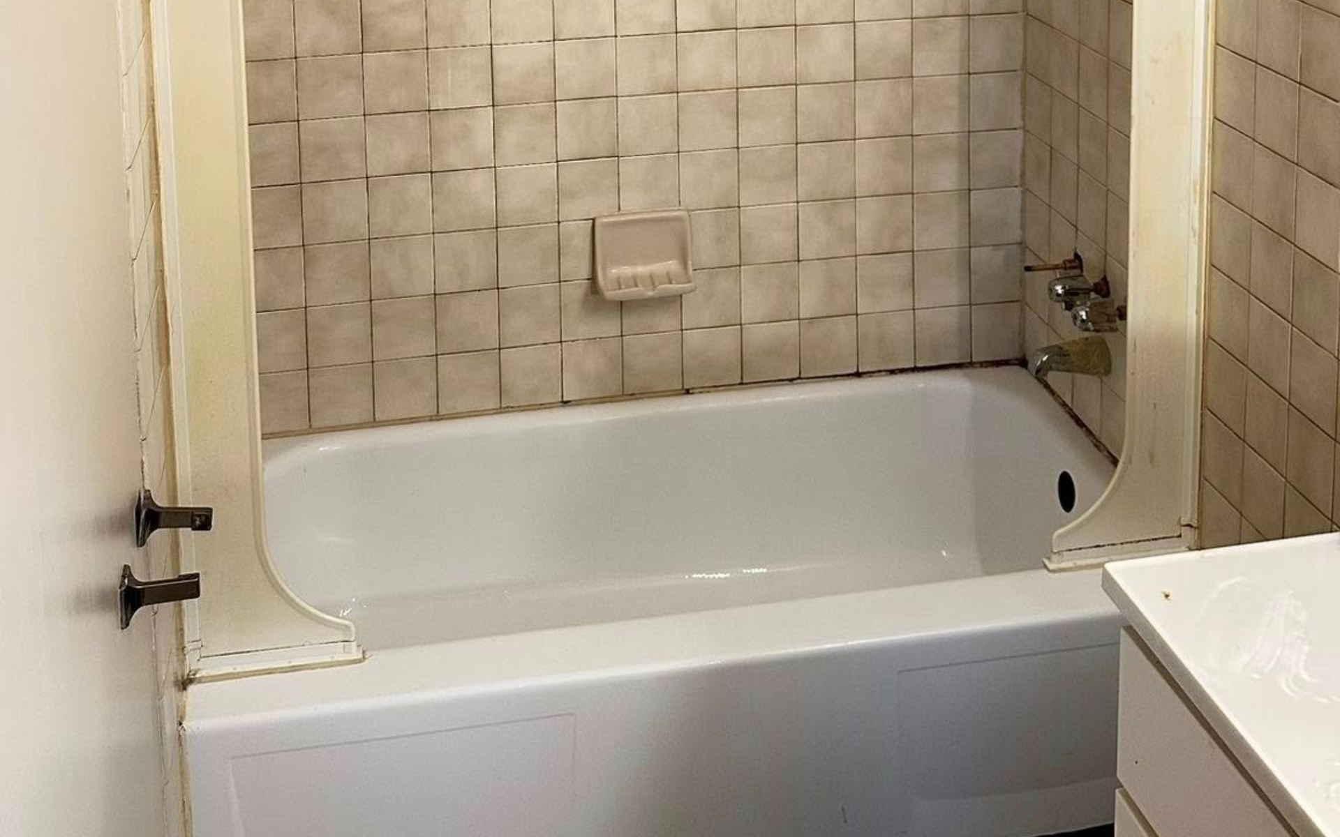 Bathroom with beige tiled walls, white tub, and shower fixtures.