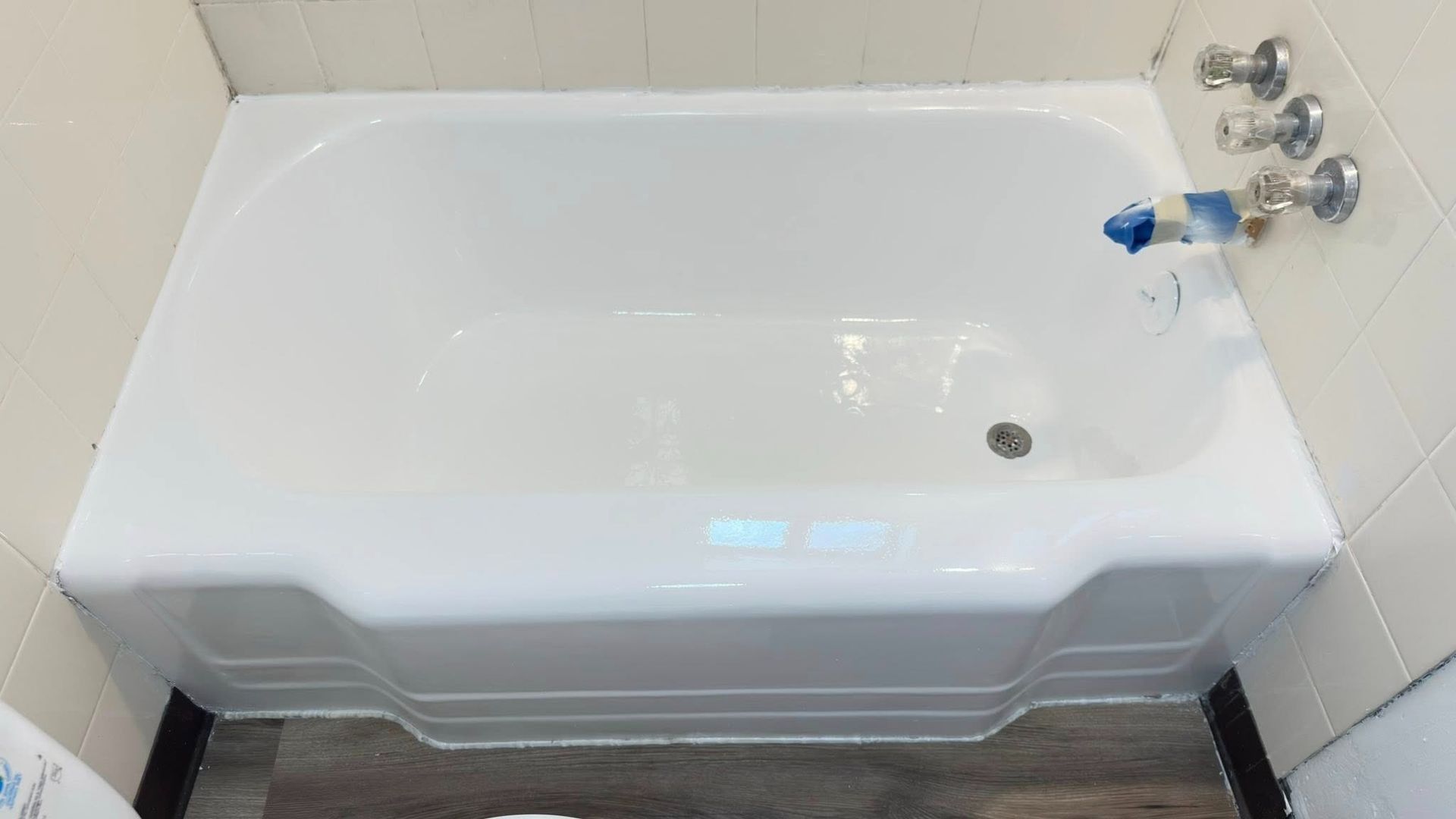 White bathtub set into a bathroom, with chrome faucets and drain.