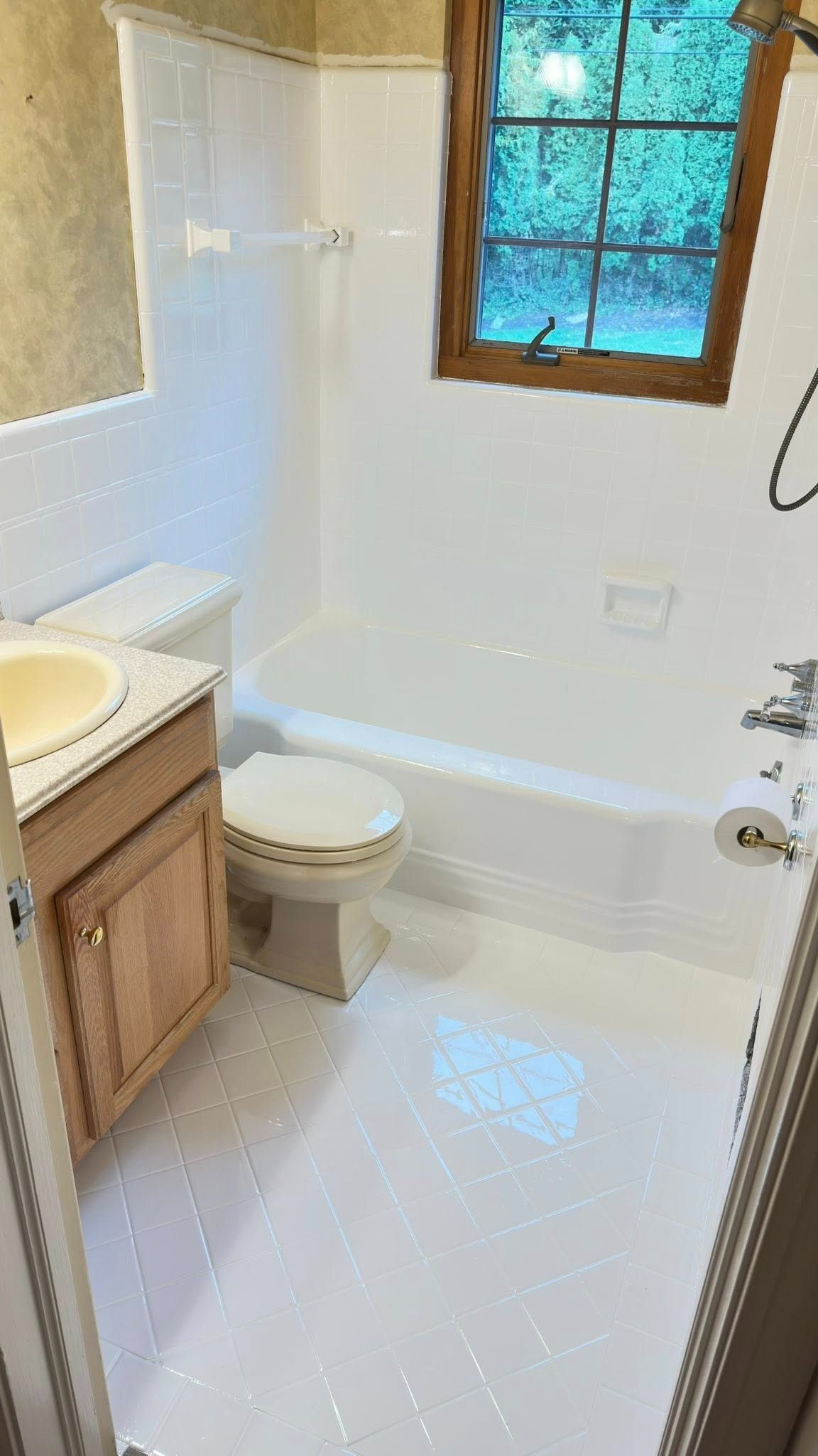 Small bathroom with a toilet, sink, and bathtub, all in white. A window provides natural light.