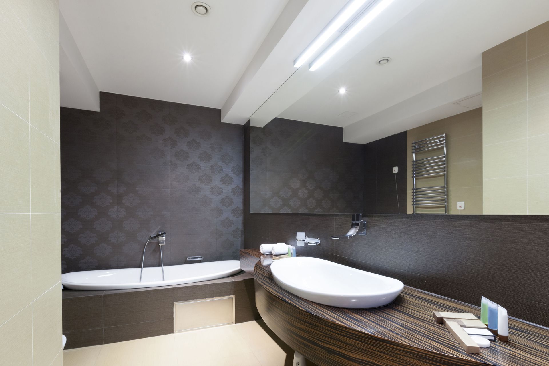Modern bathroom with tub, vessel sink, and large mirror; dark patterned wall and beige walls.