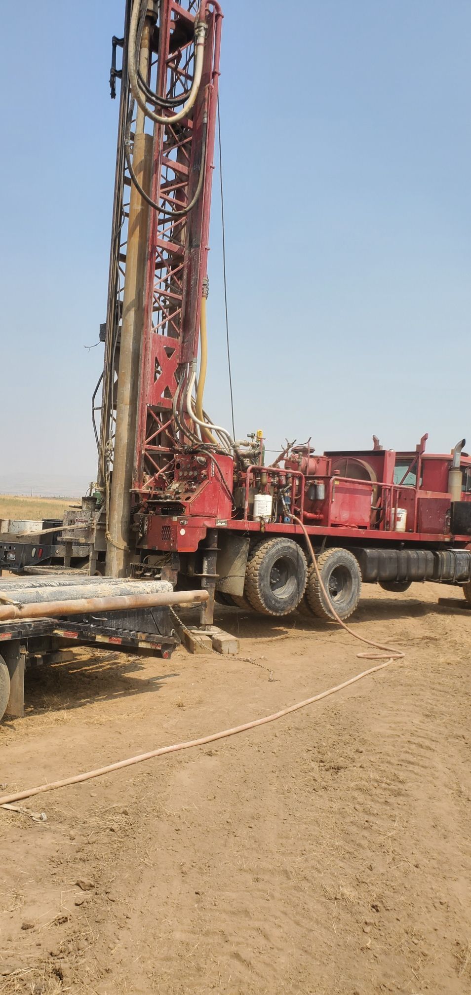 Red drilling rig truck parked on a sandy construction site under a clear sky
