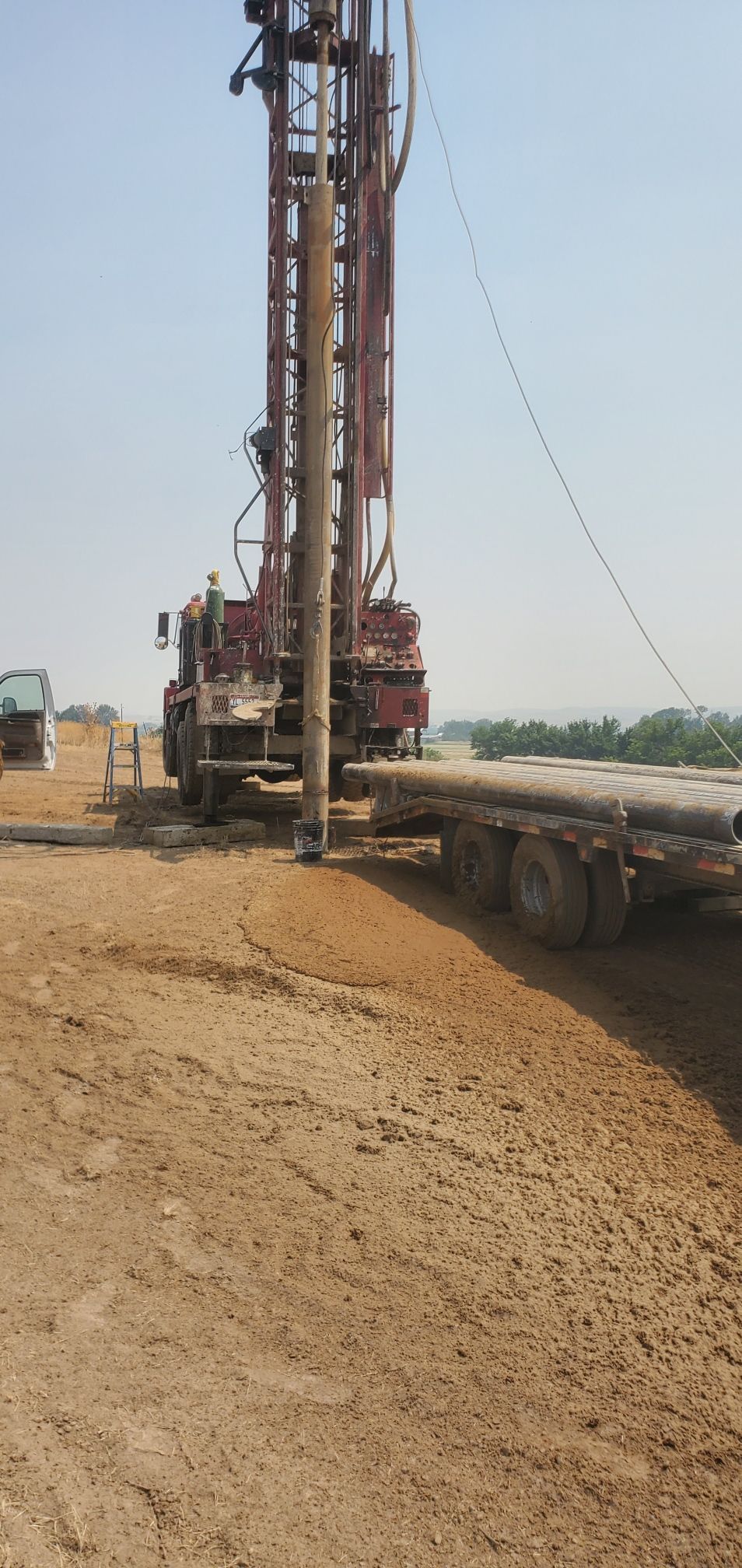 Drilling rig beside a truck on a dirt construction site under a clear sky