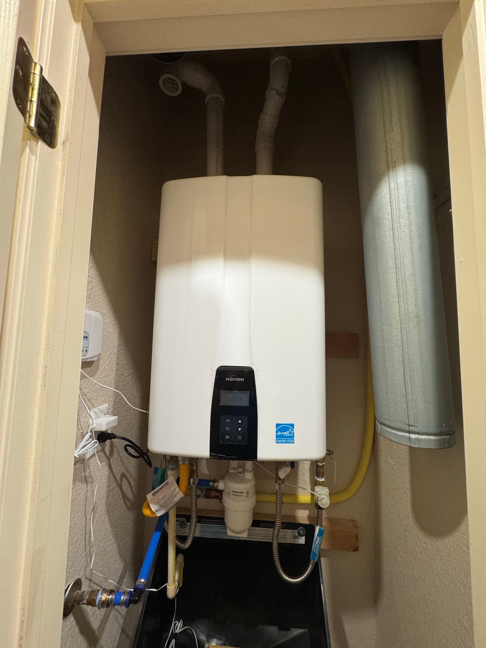 White tankless water heater installed in a small utility closet with venting and water pipes.