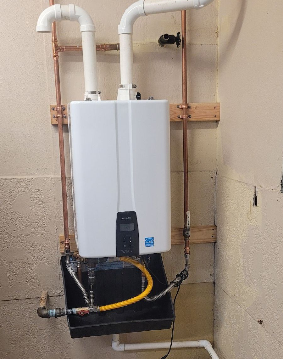 White tankless water heater with white and copper pipes against a wall.